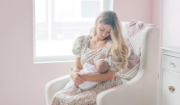Woman breastfeeding her baby while sitting on a rocking chair and wearing a nusring-friendly dress with nursing zippers